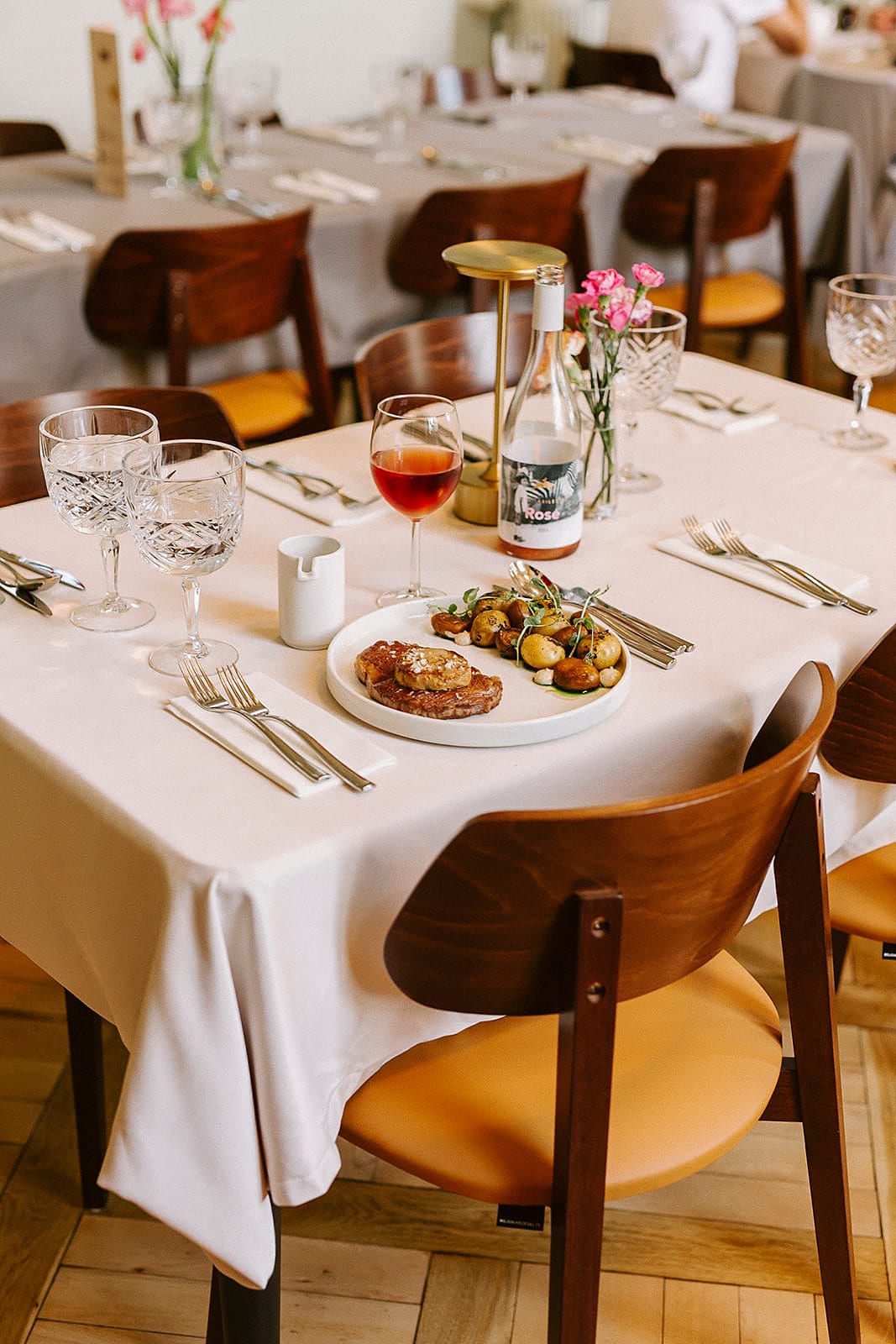 Stół z daniem i kieliszkiem różowego wina między drewnianymi krzesłami w sali restauracji